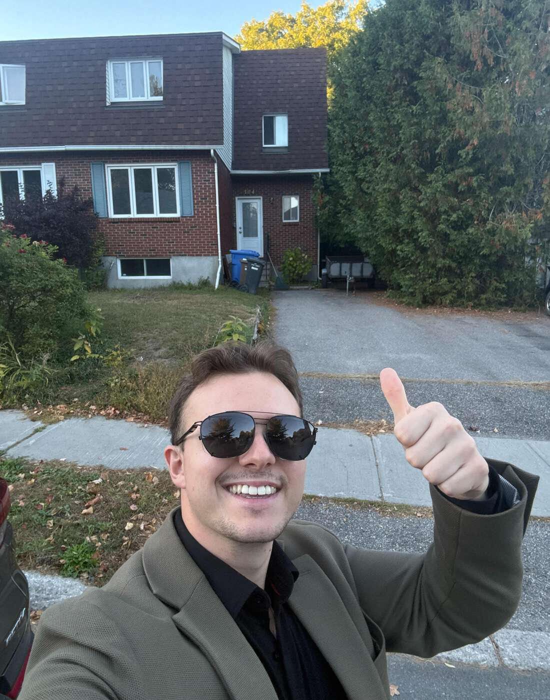 Justin Sirois, pouce levé, devant une maison d'un quartier résidentiel
